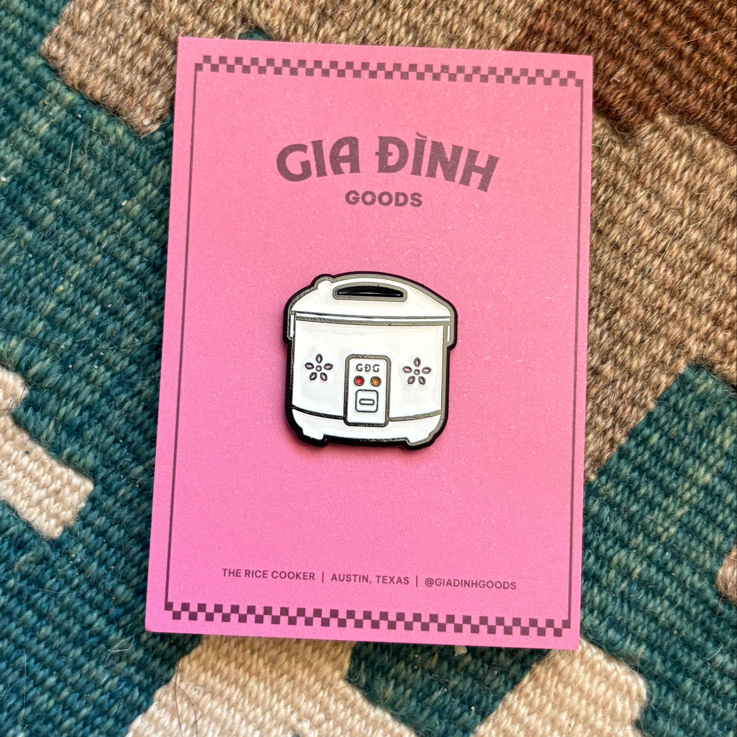 Rice cooker in on rug with a pink backing card